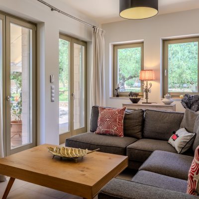 A cozy living room in Olive Grove villa, featuring a couch, coffee table, and a large window with natural light.