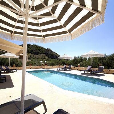 The inviting pool at Olive Grove villa, adorned with a striped umbrella and comfortable lounge chairs for relaxation.