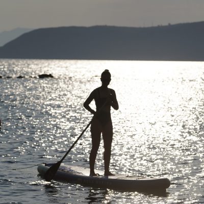 A person paddles on a paddle board in the clear waters of Kardamyli, surrounded by scenic coastal views.